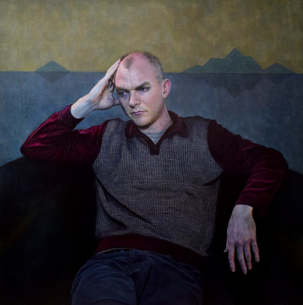 A man seated looking to the side with his head resting in his hand