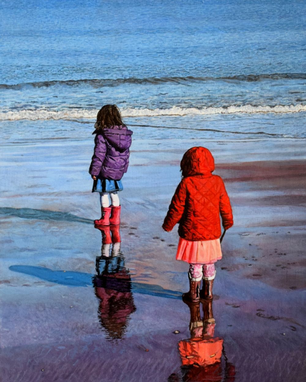 Two toddlers standing on the beach with their back to the viewer looking at the sea