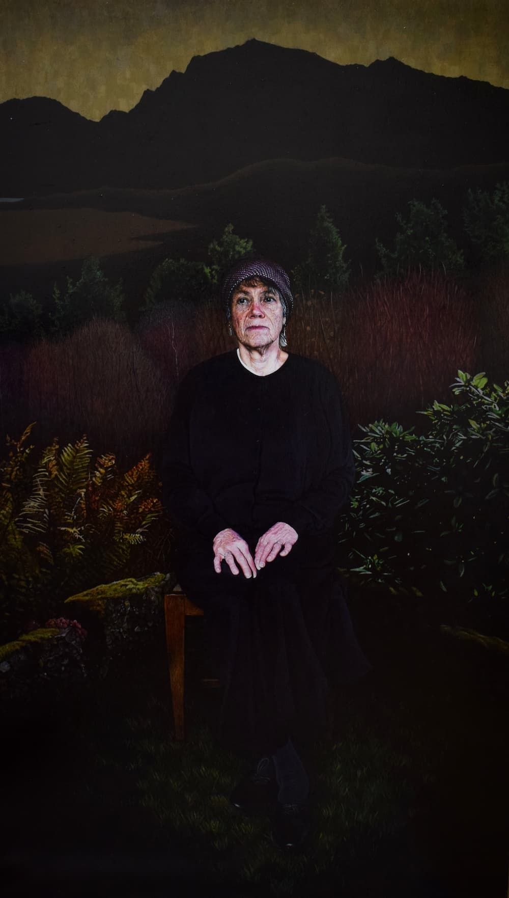 Woman sitting with her hands on her lap in a garden with a mountain silhouette in the background