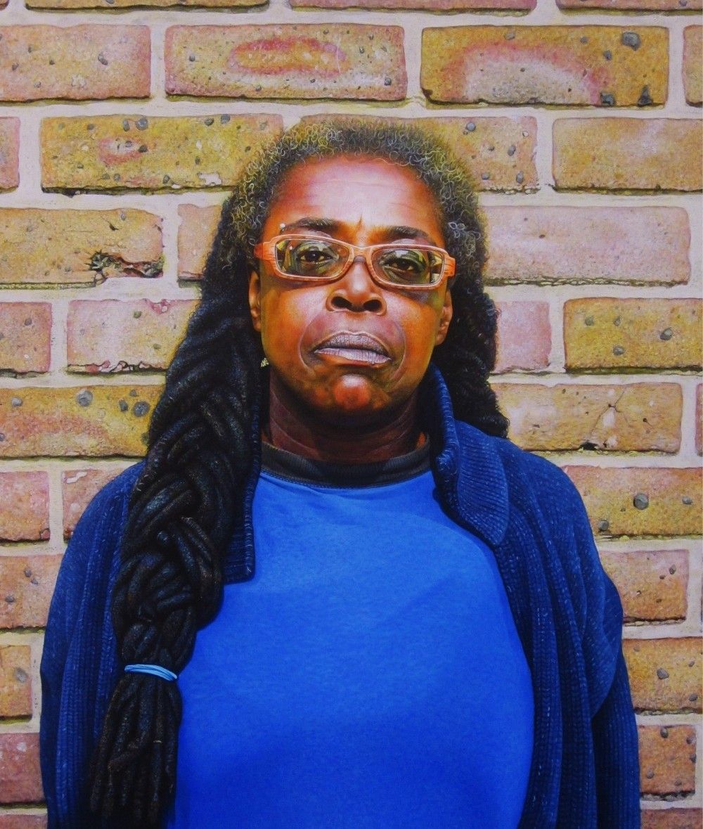 A woman with a long dreadlocked pleat standing in front of a brick wall