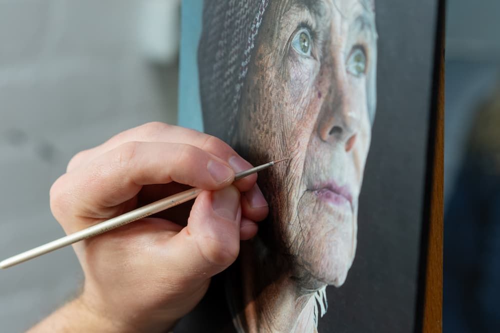 Close up of a hand holding a paint brush working on a portrait